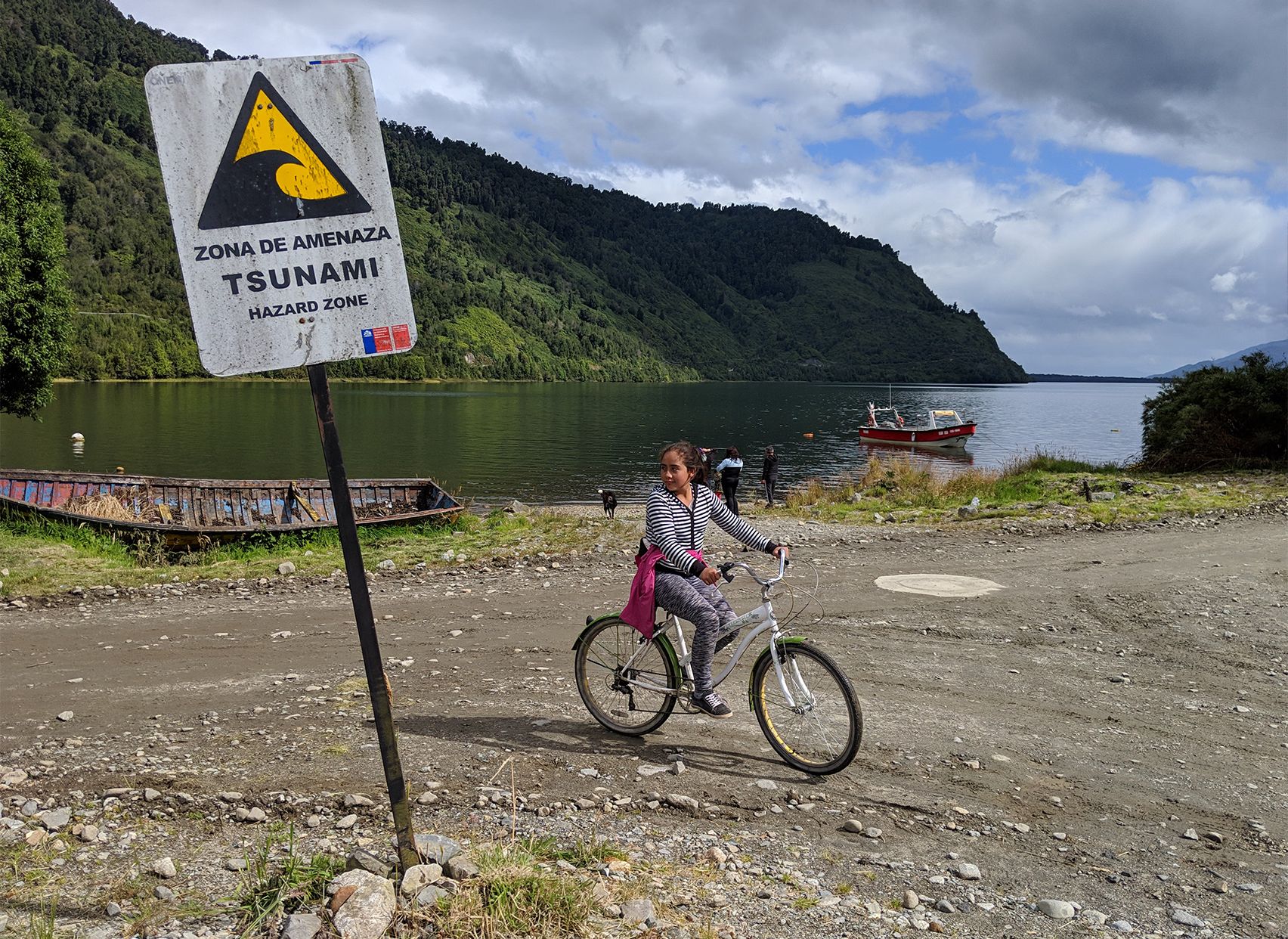 Girl riding bike next to a Tsunami warning sign